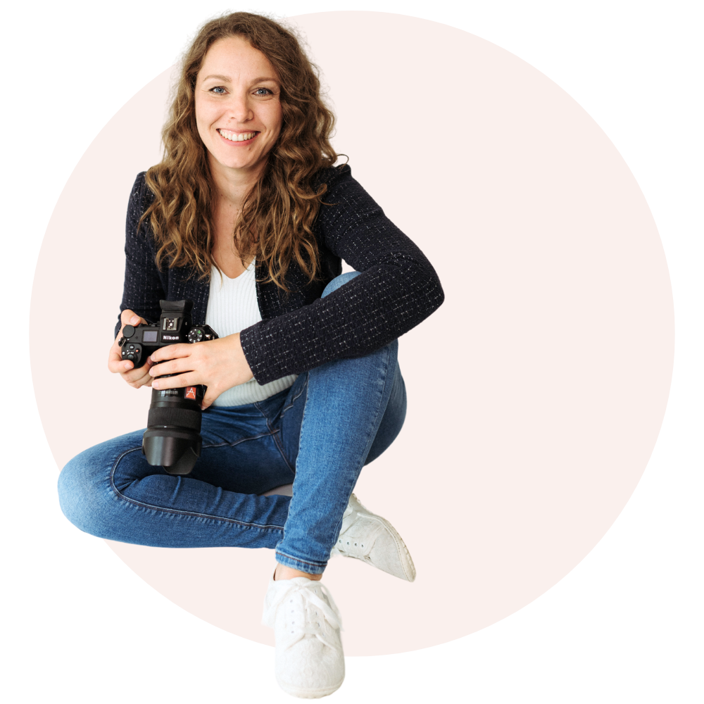 Eine lächelnde Person hält eine Kamera und sitzt auf dem Boden.