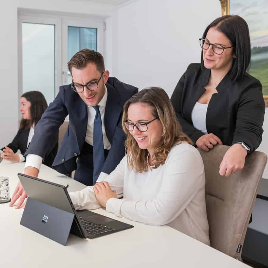 Das Bild zeigt drei Personen in professioneller Kleidung, die zusammenarbeiten und lächelnd einen Laptop betrachten.