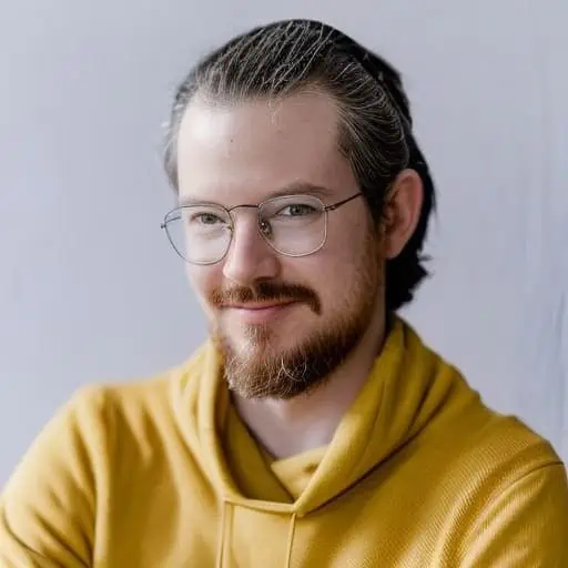 Es ist ein Porträt eines lächelnden Mannes mit Brille und Bart, der einen gelben Kapuzenpullover trägt.