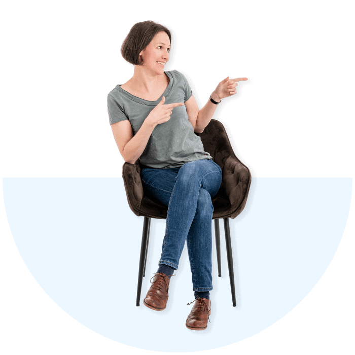 Eine lächelnde Person sitzt auf einem Stuhl und deutet mit dem Finger nach rechts.