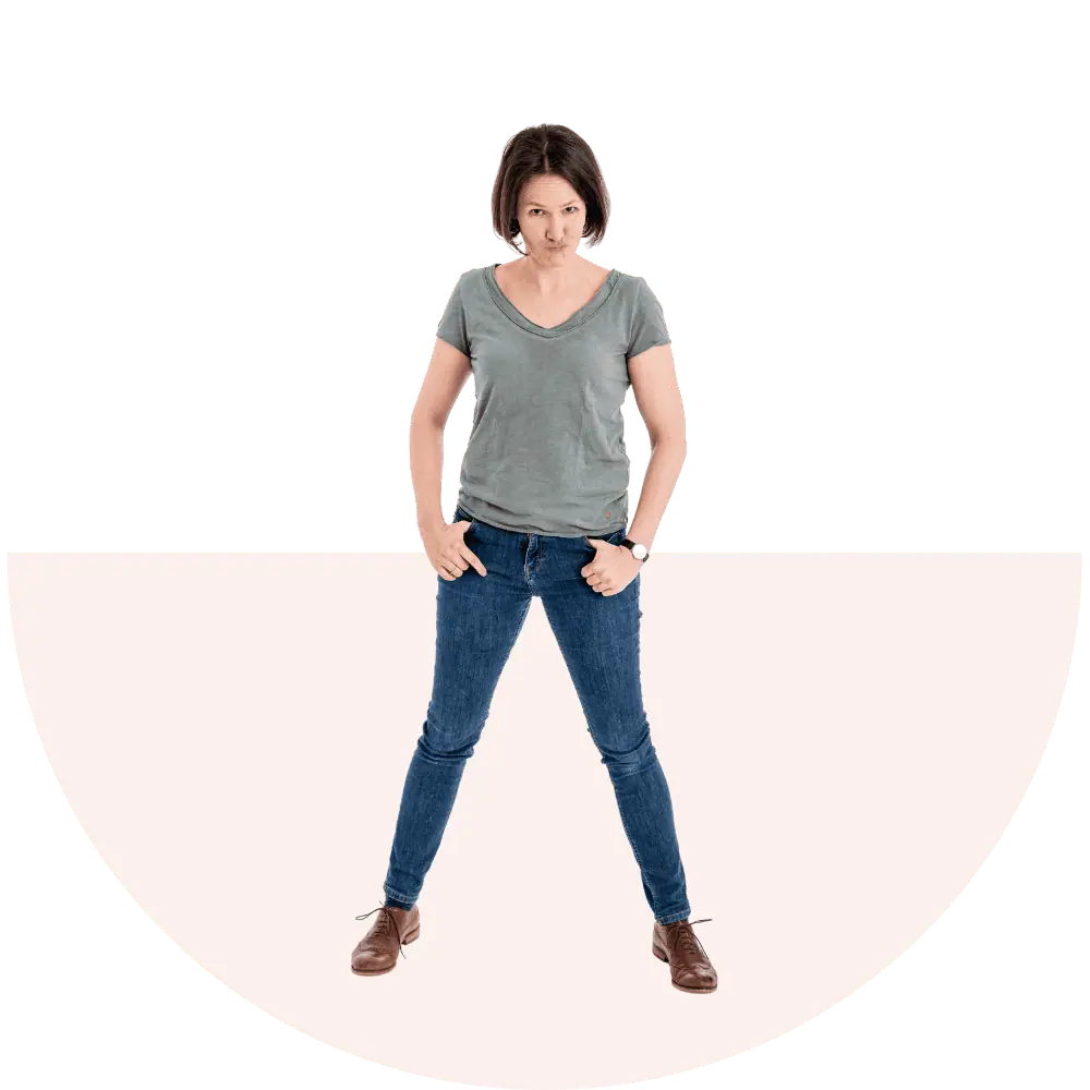 Das ist ein Bild einer Frau, die in Jeans und T-Shirt steht und direkt in die Kamera blickt.