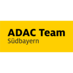 Das Bild zeigt ein Logo mit der Aufschrift "ADAC Team Südbayern" auf gelbem Hintergrund.