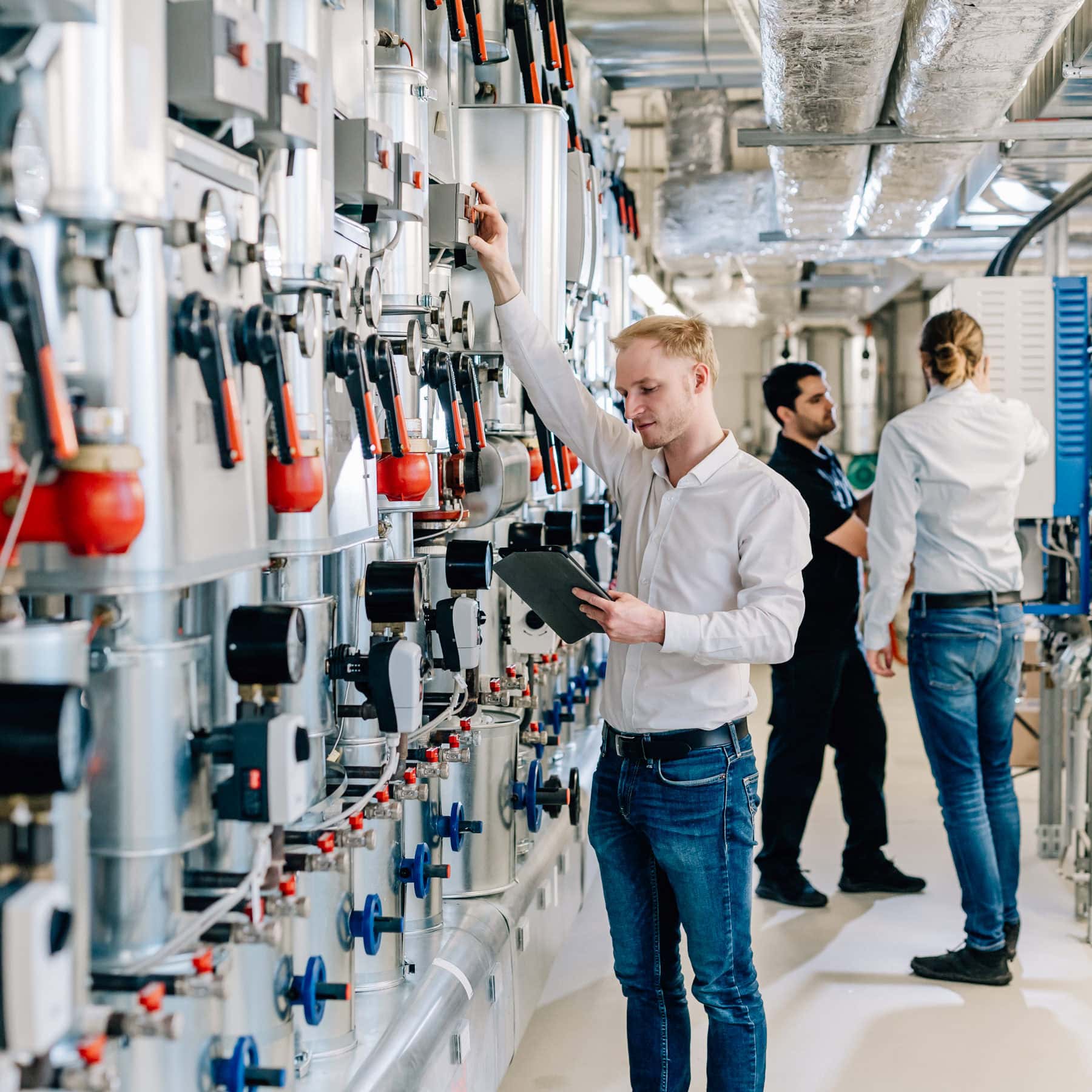 In einem modernen technischen Umfeld überwacht ein Fachkraft die Ausstattung zur Energiemessung, während zwei weitere Mitarbeiter in dieser hochentwickelten Anlage aktiv sind. Der Fokus auf Effizienz und Technologie verdeutlicht die Relevanz von Fachwissen in der Industrie 4.0.