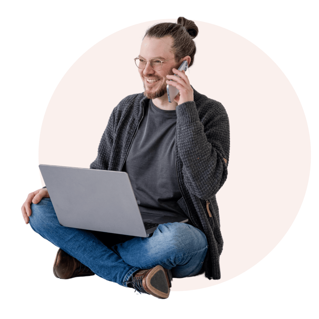 Der junge Mann sitzt entspannt auf dem Boden und führt ein Telefonat, während er an einem Laptop arbeitet, was die ideale Kombination aus Homeoffice und produktiver Kommunikation verkörpert. Diese Szene stellt modernes Arbeiten und Multitasking in einer ansprechenden, kreativen Umgebung dar und ist perfekt für Inhalte über digitales Arbeiten und flexible Lebensstile.
