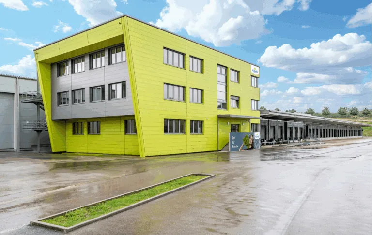 Das moderne, grüne Gebäude mit einem innovativen Design steht für frische Lebensmittelqualität und zeitgemäße Logistik. Mit einem hellen, einladenden Layout und funktionalen Anlieferungen ist es ein wichtiger Standort für effiziente Warenverteilung und nachhaltige Geschäftspraktiken.